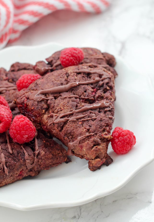 A white plate with paleo chocolate raspberry scones on it with fresh raspberries on top.