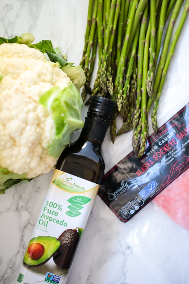 Avocado oil, cauliflower, aspargus and salmon all lying out on a counter before cooking it.