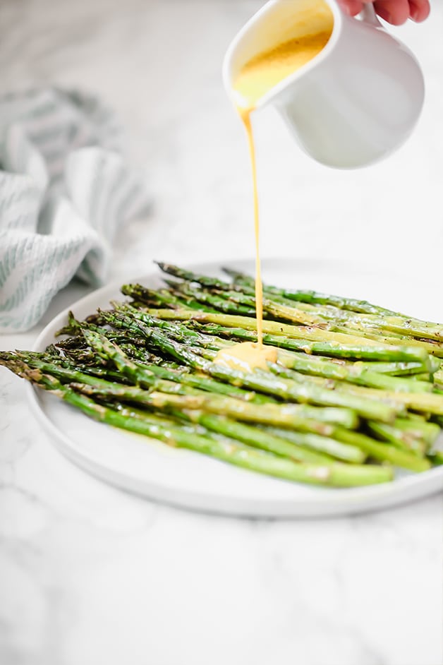 A white plate filled with roasted asparagus with a sauce drizzling over it.