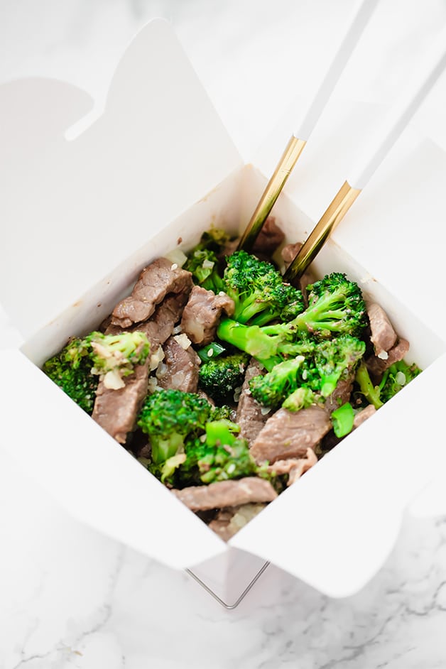 A white takeout container filled with beef and broccoli and chop sticks in it.