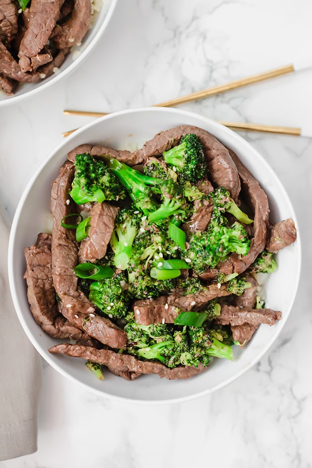 A white bowl with beef and broccoli stir fry in it with chop sticks next to it.