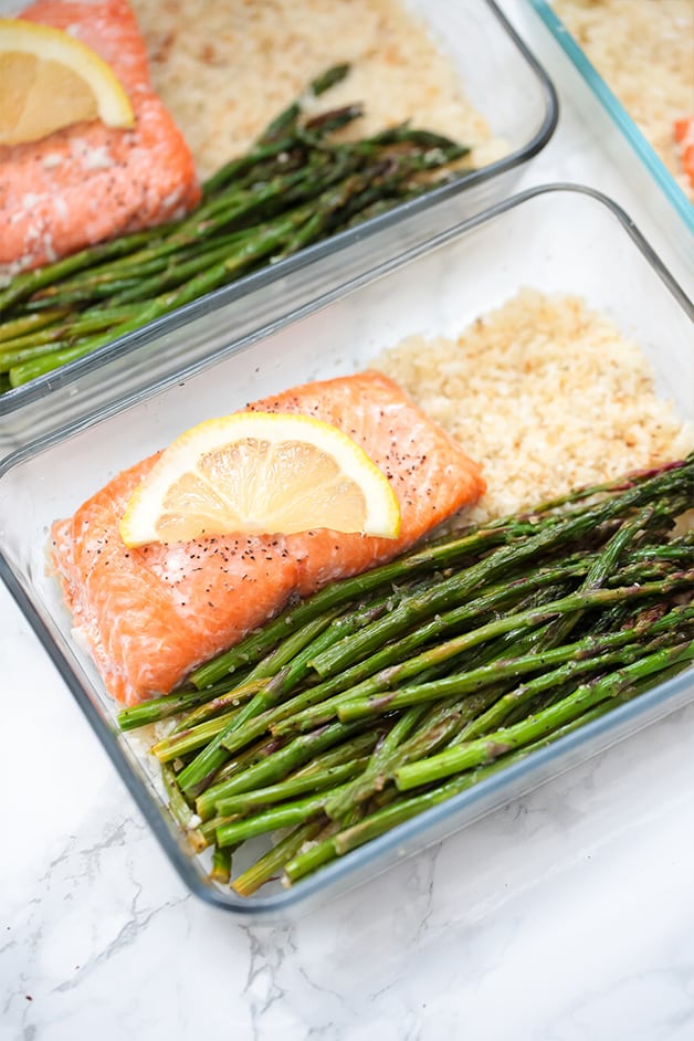 A glass meal prep container filled with roasted aspargus, salmon, and cauliflower rice.