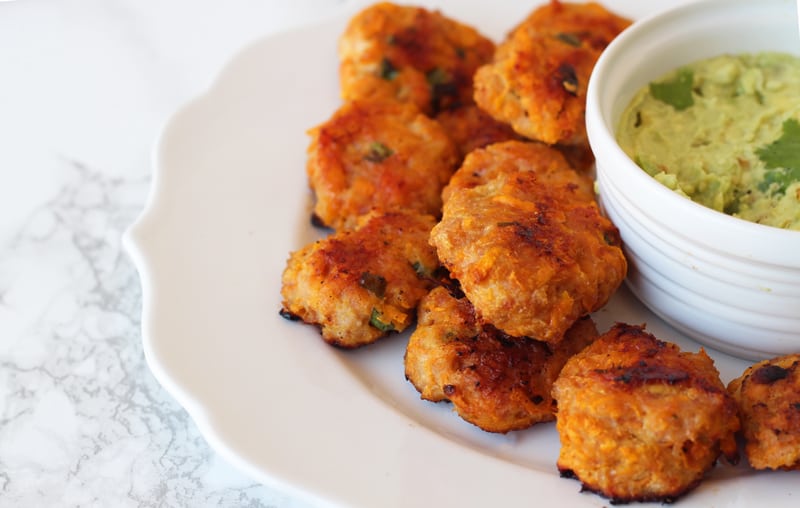 A white plate with sweet potato chicken poppers on it and dipping sauce.