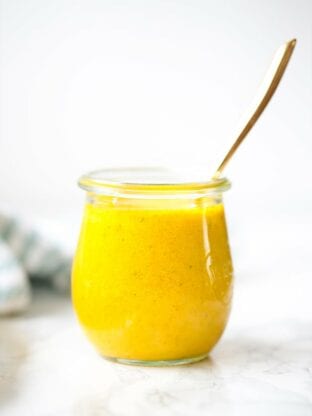 A class jar filled with turmeric dressing and a spoon sticking out of it.