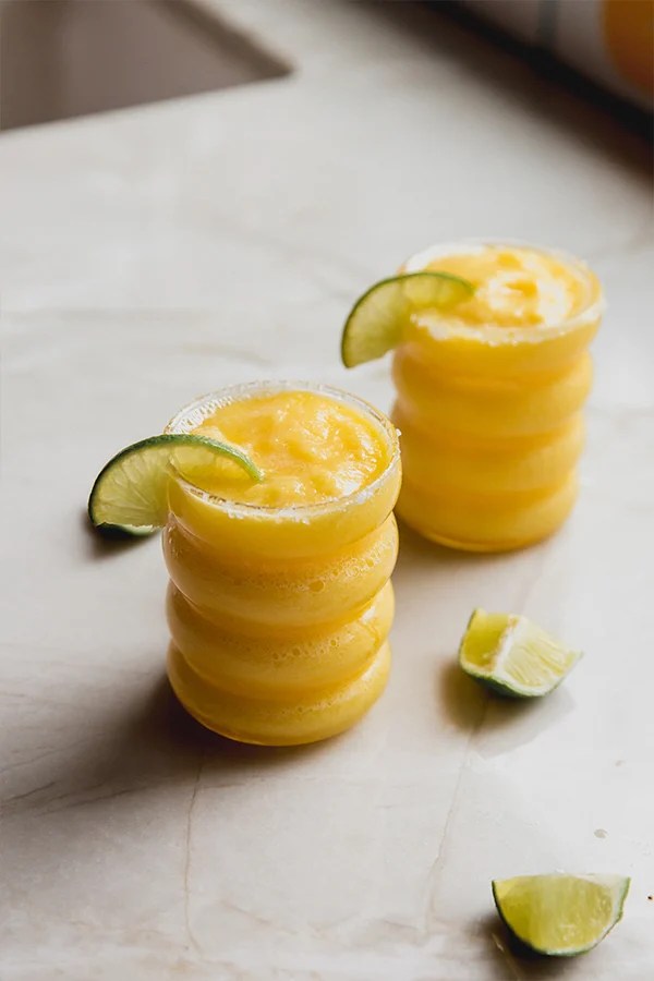 Two glasses of frozen mango margarita mocktail with lime slices.