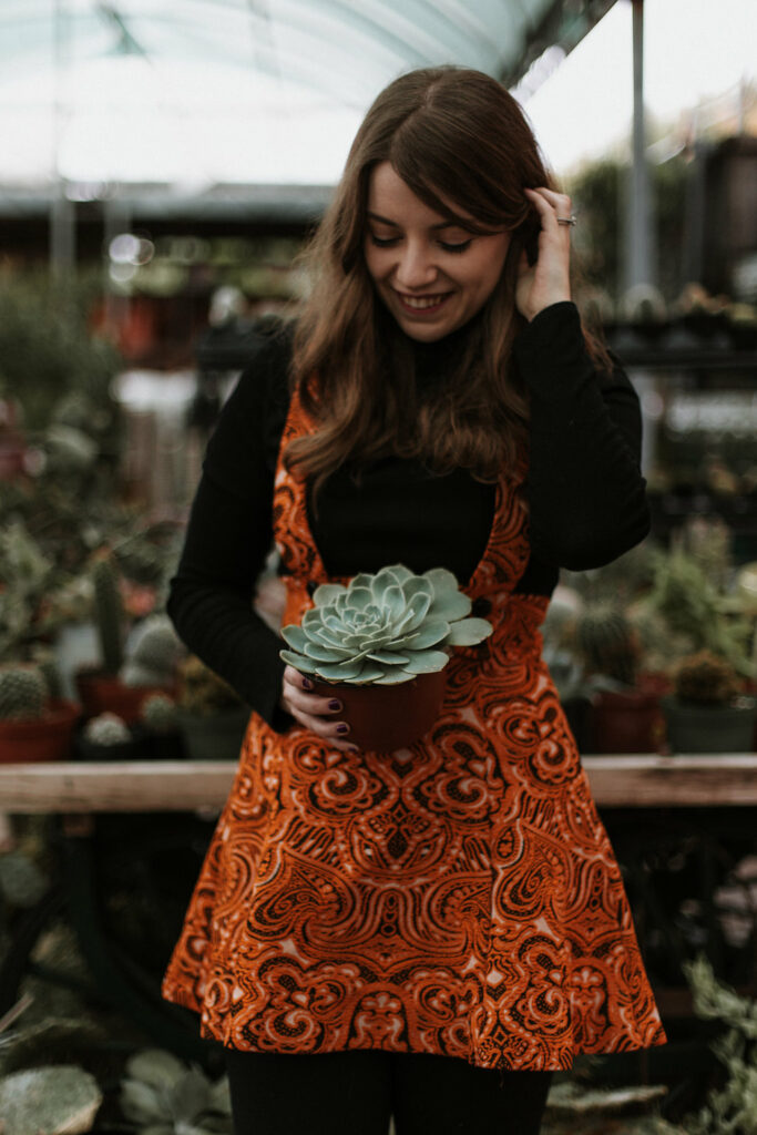Michelle holding a succulent plant dressed in a black long sleeve top and orange dress.