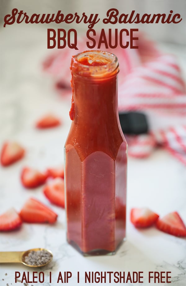 A glass bottle of strawberry balsamic BBQ suace on a counter with cut up strawberries around it.