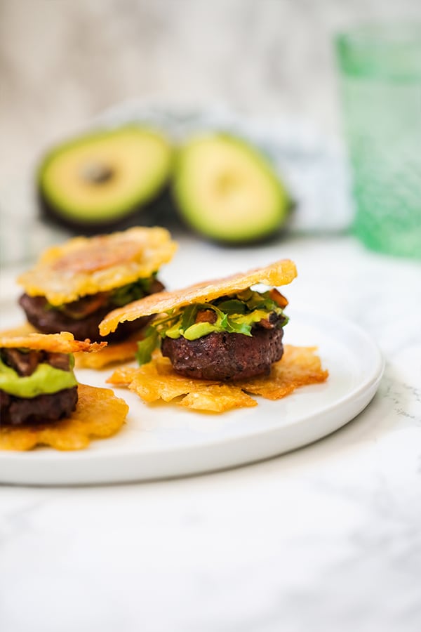 Three tostone slider on a plate topped with avocado and greens, and with an avocado behind it.