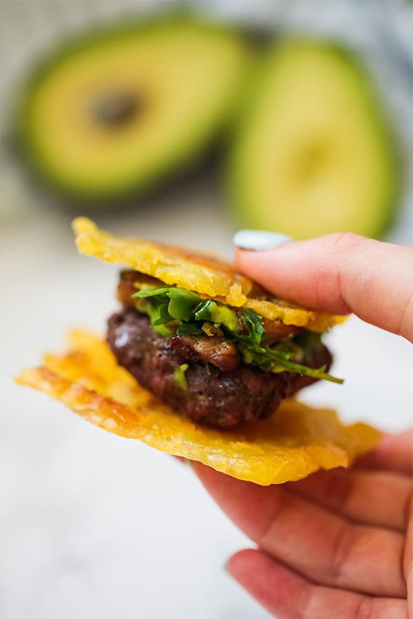 A hand holding a slider on a plantain tostone bun.