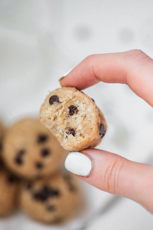 A hand holding a cookie dough collagen protein bites with a bite taken out of it.