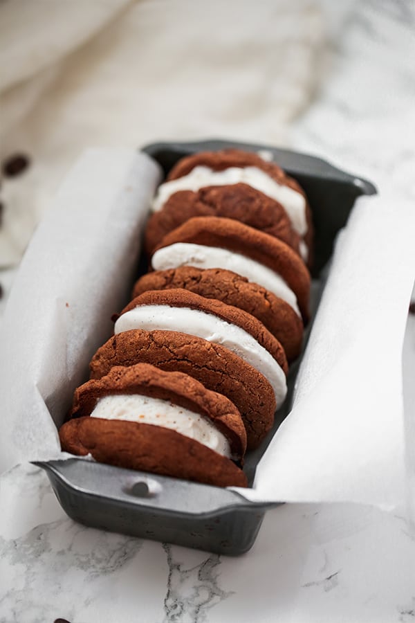 A stack of three ice cream sandwiches in a loaf pan with parchment paper.