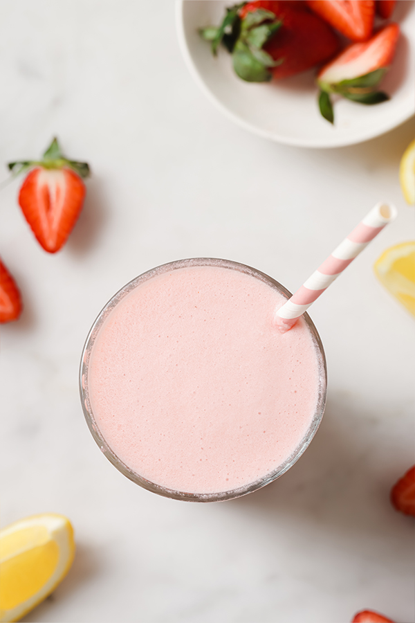 Glass of creamy frozen pink lemonade on a table with fruit.