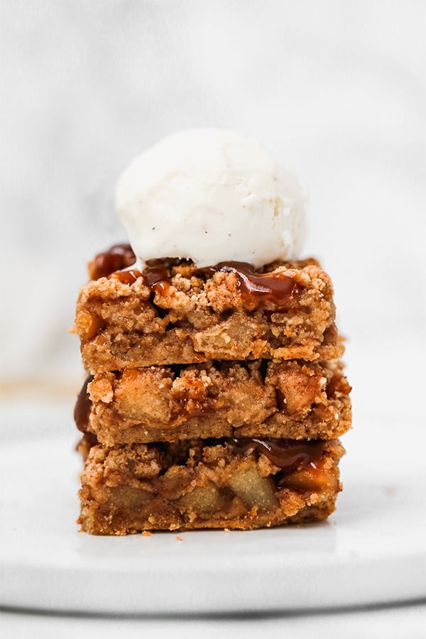 A stack of three apple pie bars topped with a scoop of vanilla ice cream.