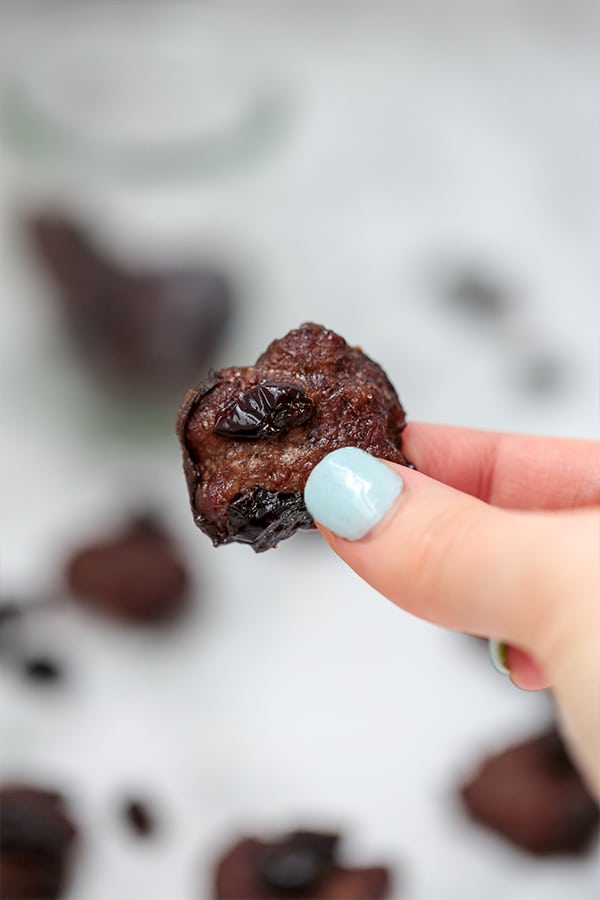 A hand with blue nails holding a beef jerky bite.