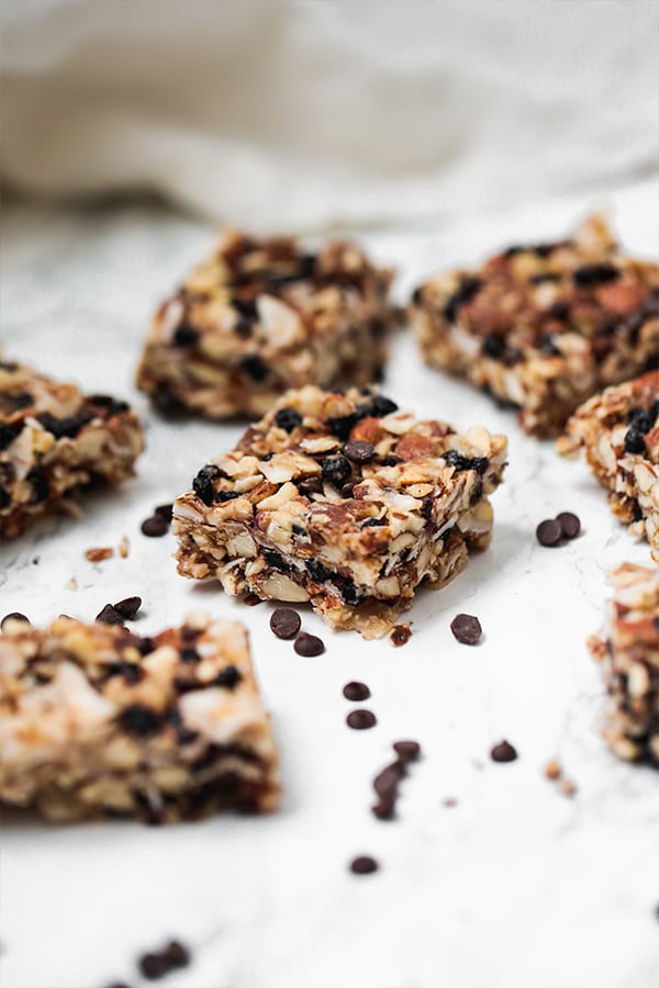 Seven granola bar pieces spread around on a counter with extra chocolate chips nearby.