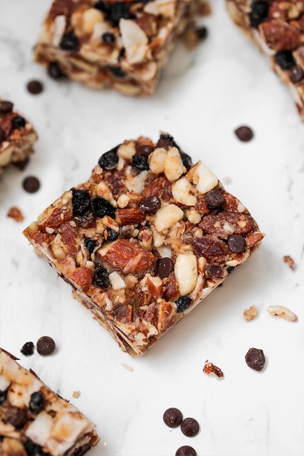 A granola bar on a counter with extra nuts and chocolate chips around.