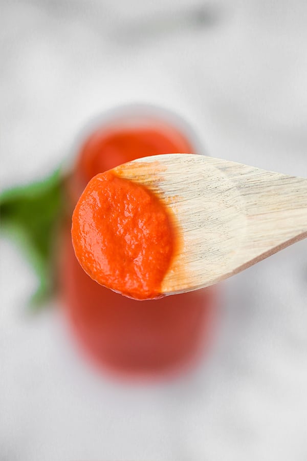 A wooden spoon taking a little bit of nightshade free marinara sauce out of the glass bottle of it.