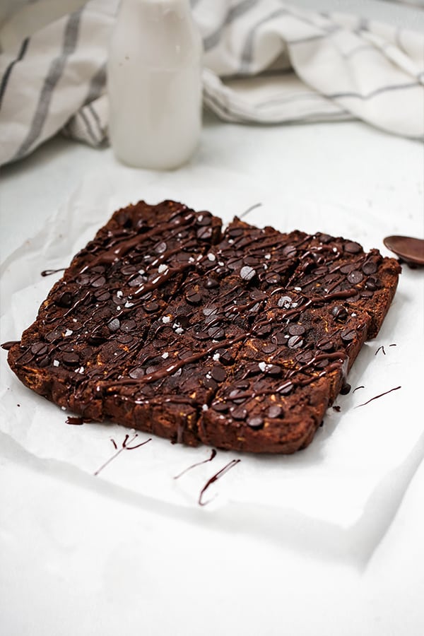 A pan of zucchini brownies cut into squares and sitting on a piece of parchment paper on a countertop.