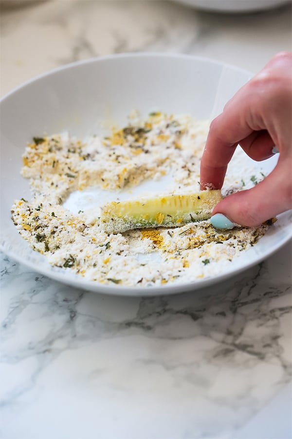 A slice of zucchini being coated in seasoning by a hand.
