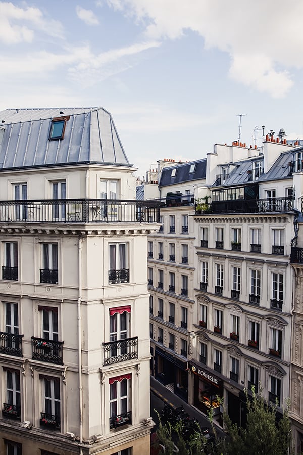 Two buildings in paris with balconies, and grey rooftops.