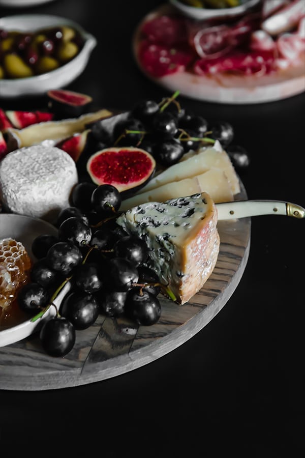 A cheese plate with cheese wedges, black grapes, figs and honeycomb