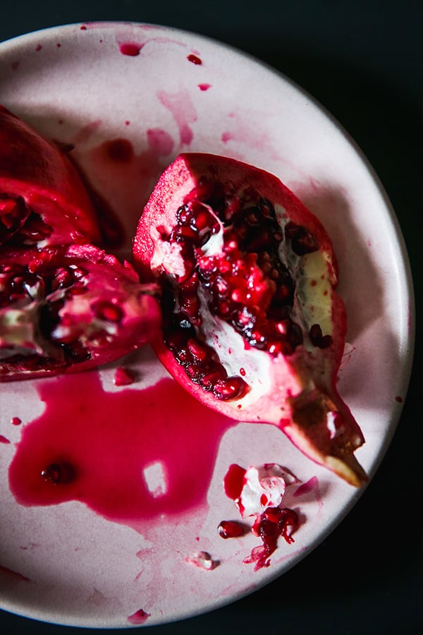 A white plate with two sections of pomegranate slices open and juice on the plate as well.