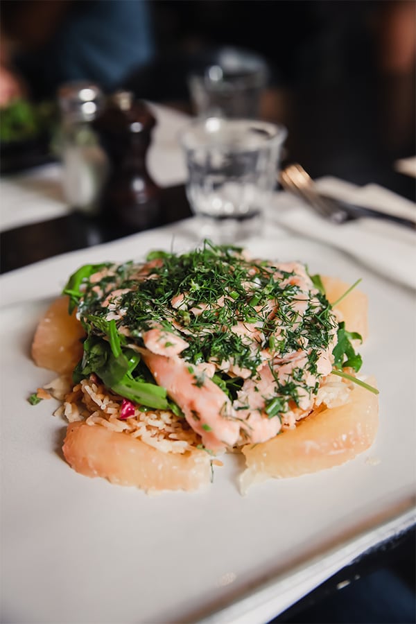 A plate of a salmon dish with grapefruit, rice, salmon, herbs, and water in the background
