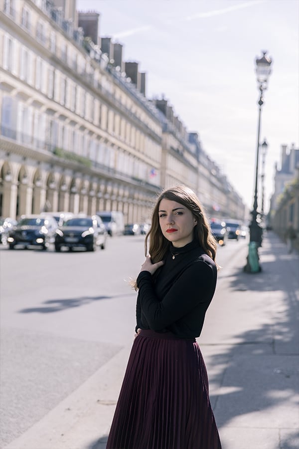 Food blogger Michelle Hoover on a street in paris, with brunette hair and a black shirt with cars and buildings in the background
