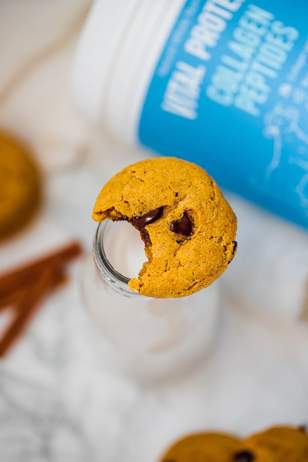 A pumpkin chocolate chip cookie balanced on the top of a glass with a bite taken out of the cookie.