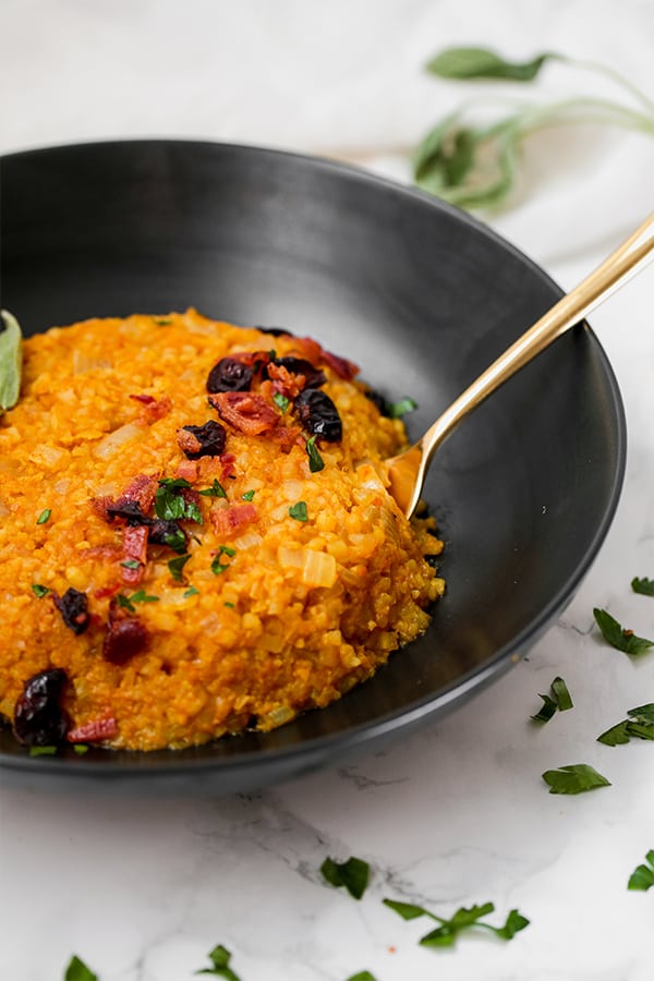 A black bowl filled with cauliflower pumpkin risotto with a spoon resting in it.