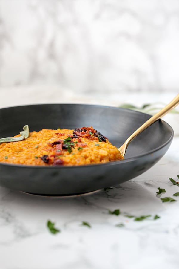 A black bowl filled with pumpkin risotto with a metal spoon in it.