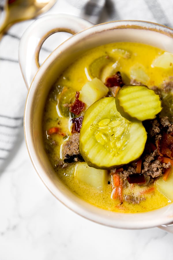 A white bowl filled with bacon cheeseburger soup topped with extra pickles