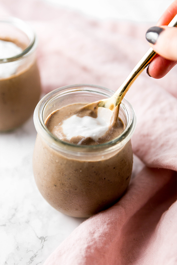A glass jar of peppermint mocha collagen pudding with whipped coconut cream on top and a spoon taking a spoonful out.