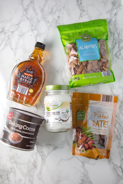 Packages of maple syrup, coconut oil, baking coco, almonds, and dates out on a counter before baking.
