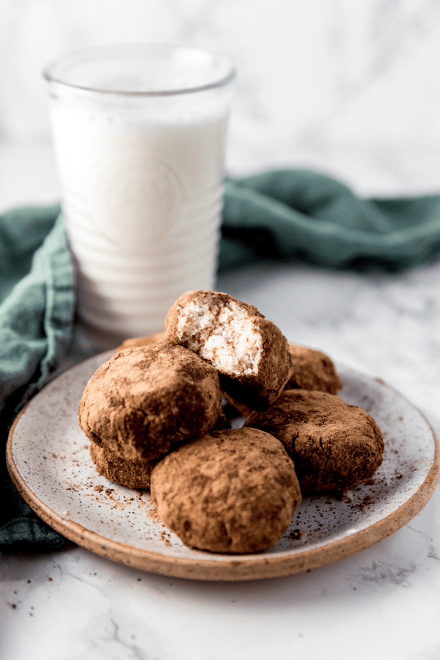 A white plate with paleo cookies on it and a class of almond milk next to it.