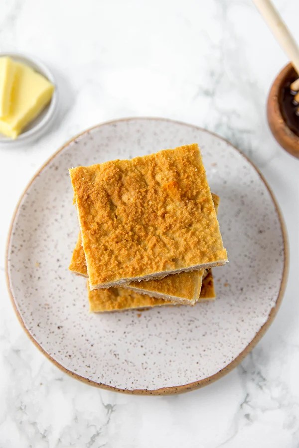 A grey plate with a stack of grain free cornbread squares stacked on it with butter nearby.