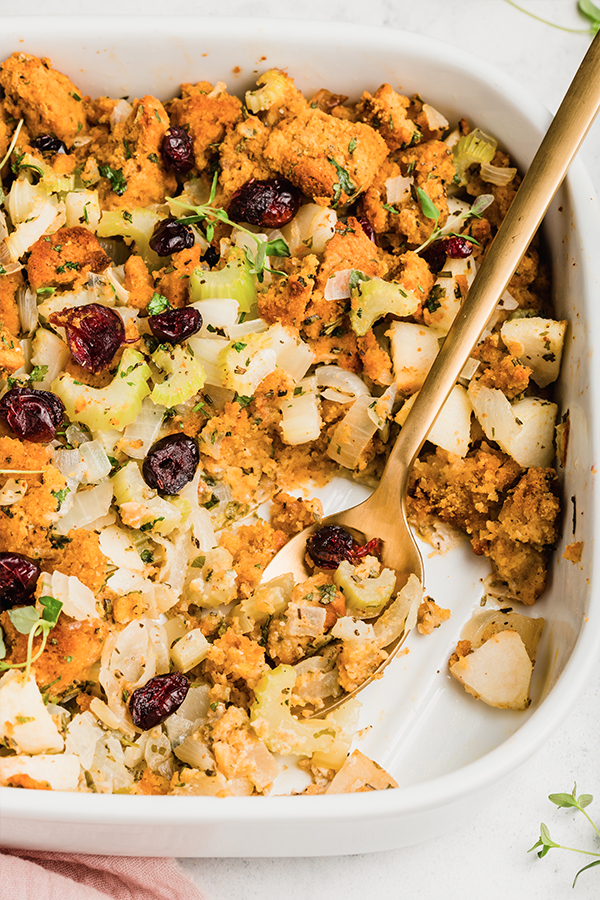 A close-up of a platter of cornbread stuffing with a serving spoon.