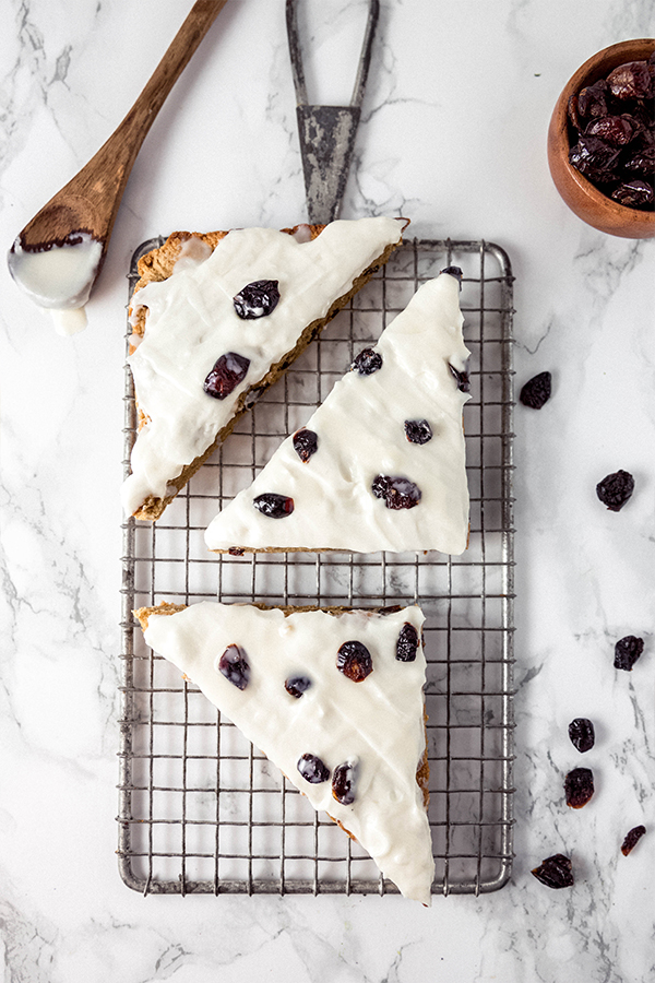 A wire cooling wrack with three cranberry bliss bars on top and extra cranberries on the counter.