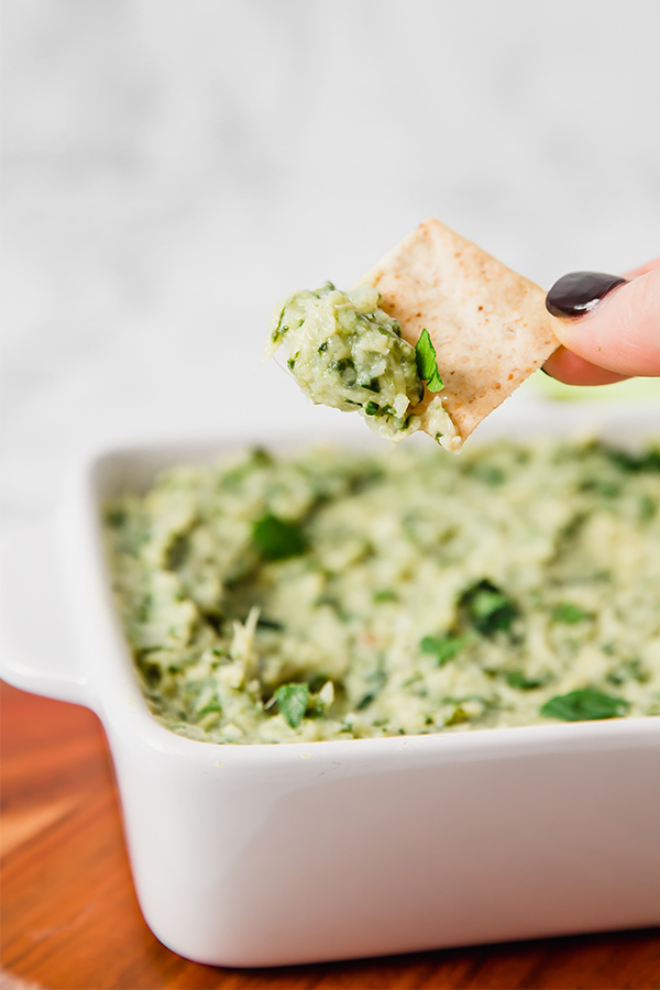 Person holding a chip dipped in spinach and artichoke dip.