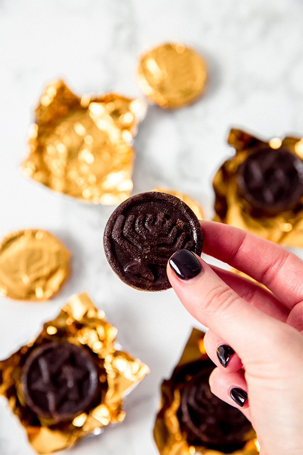 A hand holding a piece of Hannukah gelt in a gold wrapper among other pieces of gelt.