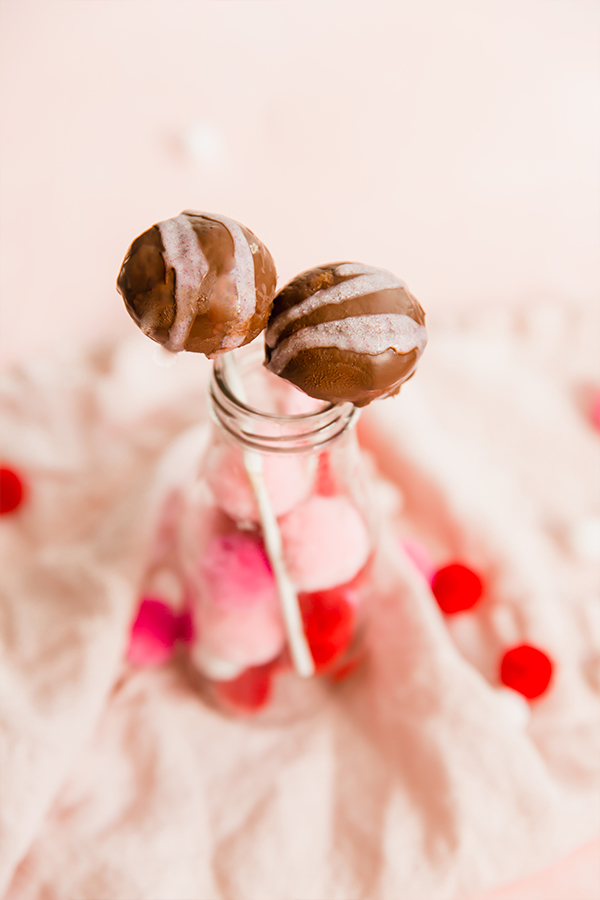 A glass jar with pink pom pomps and two cake pops in it.