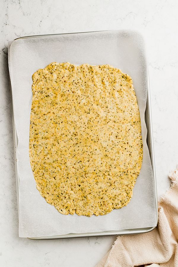 The cauliflower dough spread on a baking sheet.