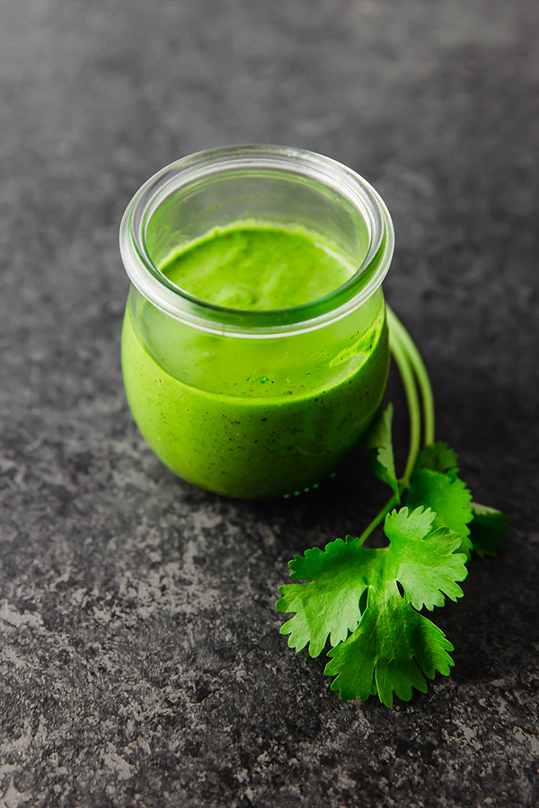 A glass jar filled with chimichurri sauce and a sprig of parsley nearby.
