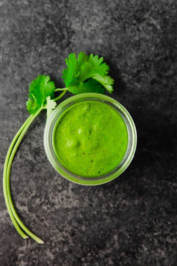 A glass jar filled with chimichurri sauce with fresh parsley next to it.