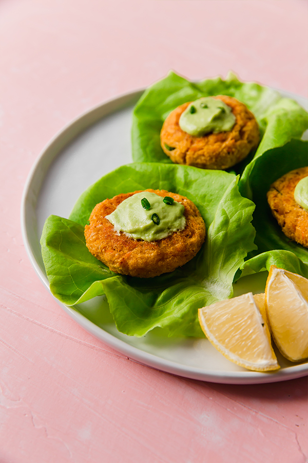 Sweet potato crab cakes on pieces of lettuce on a plate with wedges of lemon next to it.