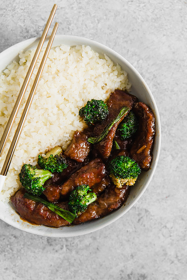 A white bowl with cauliflower rice and mongolian beef stir fry.