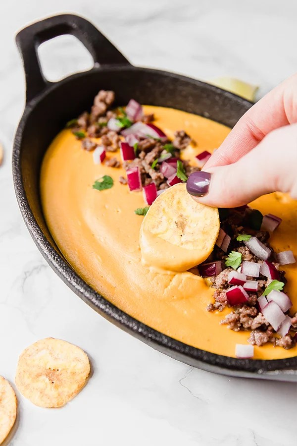Person dipping a chip into queso.