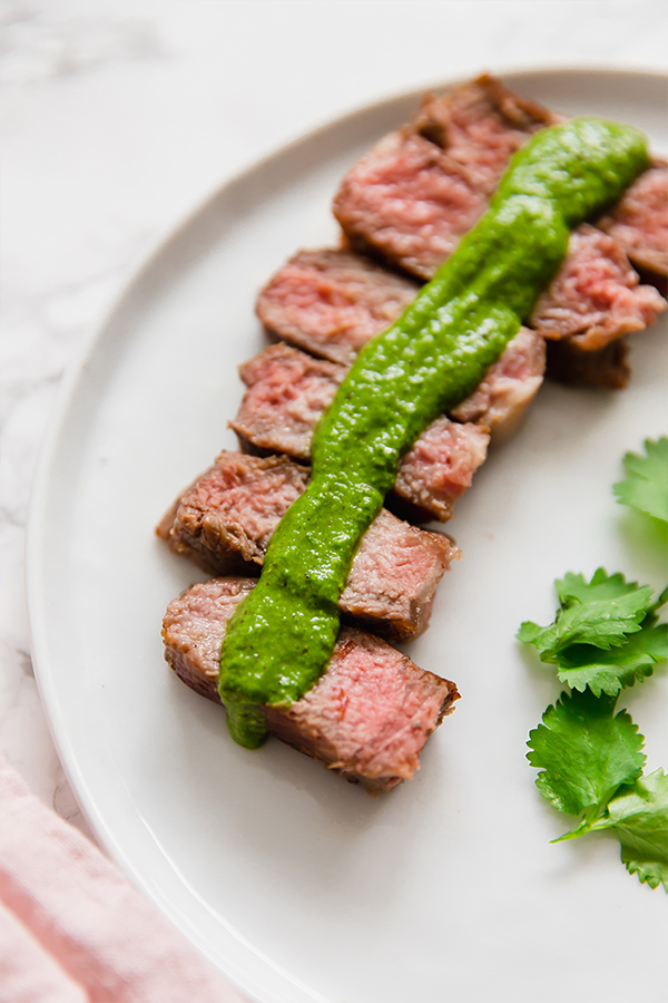 A white plate with steak topped with green sauce.