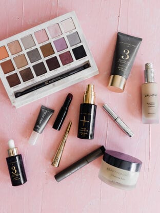 A bunch of makeup spread out on a pink background.