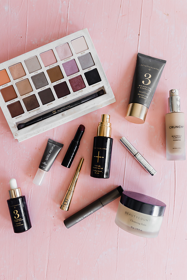 A bunch of makeup spread out on a pink background.